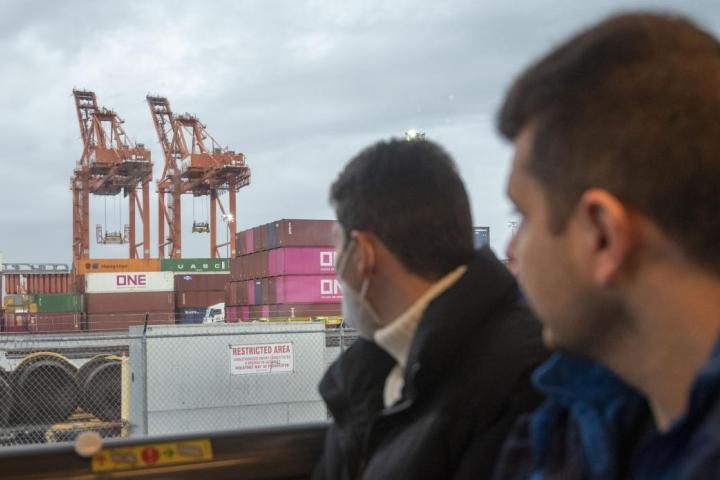 Two men looking out a bus window at some cranes. 